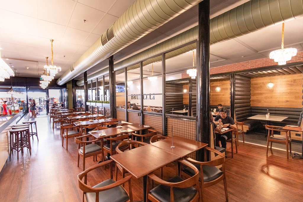 Interior view of Cafe Brunelli restaurant with wooden tables and chairs, booth seating, and exposed ceiling ducting.